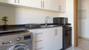 Ett modernt kök med vita skåp, en diskmaskin i rostfritt stål, en mikrovågsugn och en tvättmaskin.
