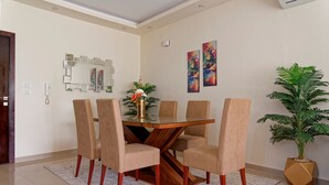 A dining area with a glass-top table, six chairs, a vase with flowers, and two wall-mounted paintings. - Vesta - Luxury APT - 2BR - La Mirada II (New Cairo)