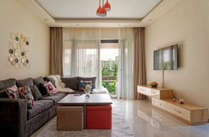 A modern living room with a sofa, coffee table, TV, and a balcony view. - Vesta - Luxury APT - 2BR - La Mirada II (New Cairo)