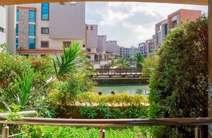 A view of a modern building complex with a bridge over a water feature, surrounded by greenery. - Vesta - Luxury APT - 2BR - La Mirada II (New Cairo)