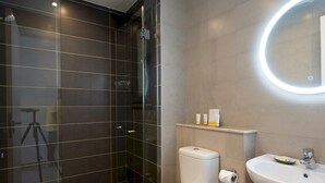 A modern bathroom with a glass shower enclosure, a toilet, a sink, and a mirror with a circular light. - Vesta - Luxury APT - 2BR - Gcribs III (El Gouna)