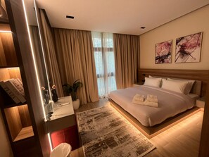 Ein modernes Hotelzimmer mit einem großen Bett, einem Nachttisch, einem Spiegel und Blick ins Freie durch das Fenster.