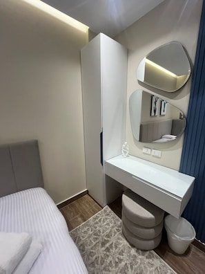 Ein modernes Hotelzimmer mit einem Bett, einem weißen Schminktisch mit Spiegel und einem grauen Kopfteil.