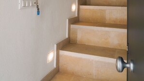 Una escalera con peldaños color beige y paredes blancas, un interruptor de luz y una puerta con pomo plateado.