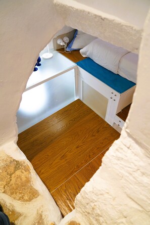 Un dormitorio pequeño y acogedor con suelo de madera, una cama con colchón azul, almohadas blancas y una mesita de noche blanca con una lámpara.
