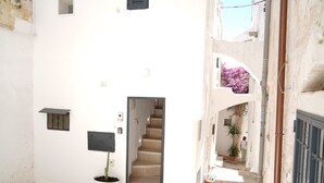 Un estrecho callejón con un edificio blanco, una planta en maceta, una puerta y una escalera que sube a otro nivel.