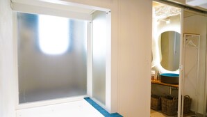 Un baño con ventana esmerilada, un lavabo con lavamanos azul y cestas de mimbre en el suelo.