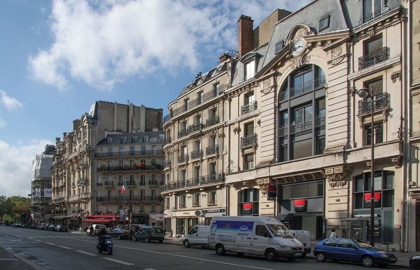 Une vue de rue avec des bâtiments historiques, un fourgon et des voitures garées.