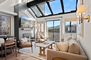 Un vaste salon doté d’un haut plafond, de grandes fenêtres et d’une vue sur les montagnes. On y trouve plusieurs coins salon, notamment un canapé et des fauteuils, ainsi qu’une table basse.