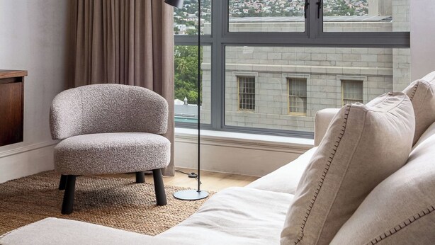 Et moderne hotelværelse med et stort vindue der viser bjergudsigt, en behagelig sofa, en mindre lænestol og en gulvlampe.