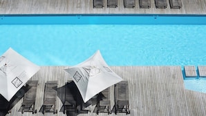 Et poolområde med træsolstole og parasoller, en træterrasse og en klar, blå pool.