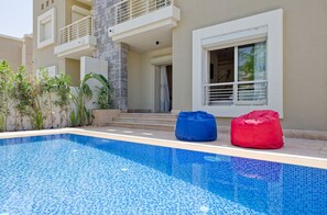 A swimming pool with blue mosaic tiles, a red bean bag, and a blue bean bag. - Vesta - Luxury Villa - 4BR - CFC (New Cairo)