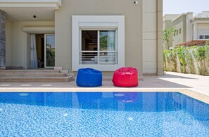 A swimming pool with two bean bags, a window, and a door leading to a balcony. - Vesta - Luxury Villa - 4BR - CFC (New Cairo)