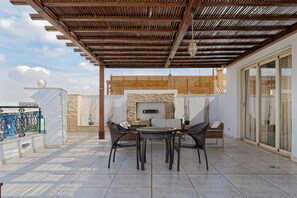 Une terrasse couverte avec une cheminée en pierre, des meubles en osier et une vue sur la ville.