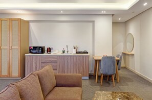 Ein modernes Wohnzimmer mit einer Couch, einem Esstisch mit Stühlen, einer Küchenzeile inklusive Geräte und einem großen Spiegel an der Wand.