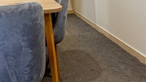 A corner room with a wooden table, a grey chair, a round mirror on a shelf, and a carpeted floor. - Vesta - Luxury Studio - New Cairo I (New Cairo)