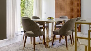 A modern dining area with a table and chairs, a chandelier, and a view of greenery outside. - Vesta - Luxury APT - 1BR - Lake View Residence (New Cairo)