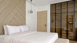 A bedroom with a large bed, a wooden accent wall, a sliding glass door closet, and a hanging pendant light. - Vesta - Luxury APT - 1BR - Lake View Residence (New Cairo)
