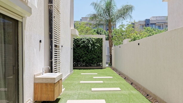 A narrow pathway with artificial grass, white stepping stones, and a wooden bench. - Vesta - Luxury APT - 1BR - Lake View Residence (New Cairo)