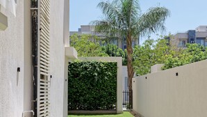 A modern outdoor area with a concrete pathway, a wooden bench, and a wall-mounted planter. - Vesta - Luxury APT - 1BR - Lake View Residence (New Cairo)