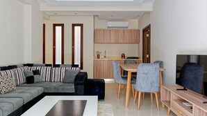 A modern living room with a grey sofa, a coffee table, and a dining area with a wooden table and chairs. - Vesta - Luxury APT - 2BR - New Cairo II (New Cairo)