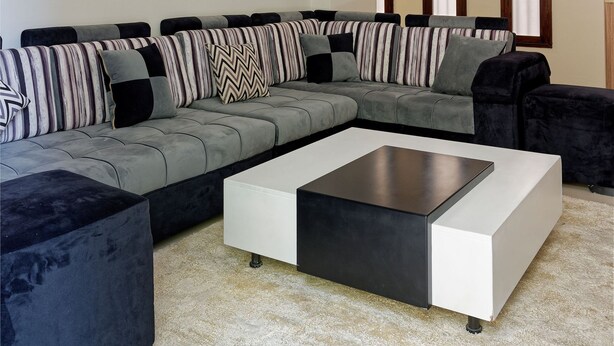A modern living room with a sectional sofa, a white coffee table, and a large window with three vertical blinds. - Vesta - Luxury APT - 2BR - New Cairo II (New Cairo)