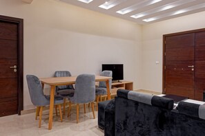 Ein Zimmer mit einem Holztisch, grau gepolsterten Stühlen, einem schwarzen Flachbildfernseher und einem dunkelgrauen Sofa.