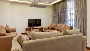 Una sala de estar moderna con un conjunto de sofás, un televisor de pantalla plana y un amplio ventanal con cortinas.