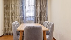 Un comedor con una mesa de madera y sillas tapizadas en gris, una araña y una ventana con cortinas.