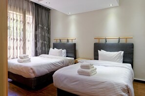 A hotel room with two beds, each with white linens and towels, a wooden headboard, and a large window with sheer curtains. - Vesta - Luxury APT - 3BR - New Cairo V (New Cairo)