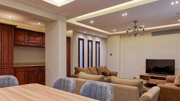 Una sala moderna con un televisor grande, sofás cómodos, una mesa de comedor y armarios de madera.