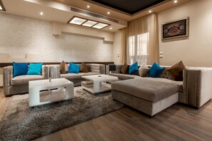 A modern living room with a sectional sofa, a white coffee table, and a large window with curtains. - Vesta - Luxury Villa - 6BR - New Cairo (New Cairo)