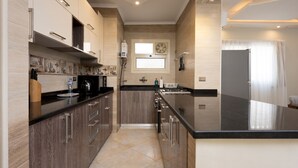A modern kitchen with dark wood cabinets, a black countertop, and a large island. - Vesta - Luxury APT - 2BR - Kattameya one (Cairo)