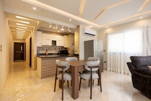 A modern kitchen with a central island, built-in cabinets, and a dining area with a table and chairs. - Vesta - Luxury APT - 2BR - Kattameya one (Cairo)