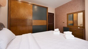 A hotel room with a large bed, a wooden wardrobe, a mirror, and a small cabinet. - Vesta - Luxury APT - 2BR - Kattameya one (Cairo)