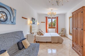 Ein Schlafzimmer mit einem Bett, einem Schlafsofa, einem Nachttisch, einem Sessel, einem Kleiderschrank und einem Bild an der Wand.