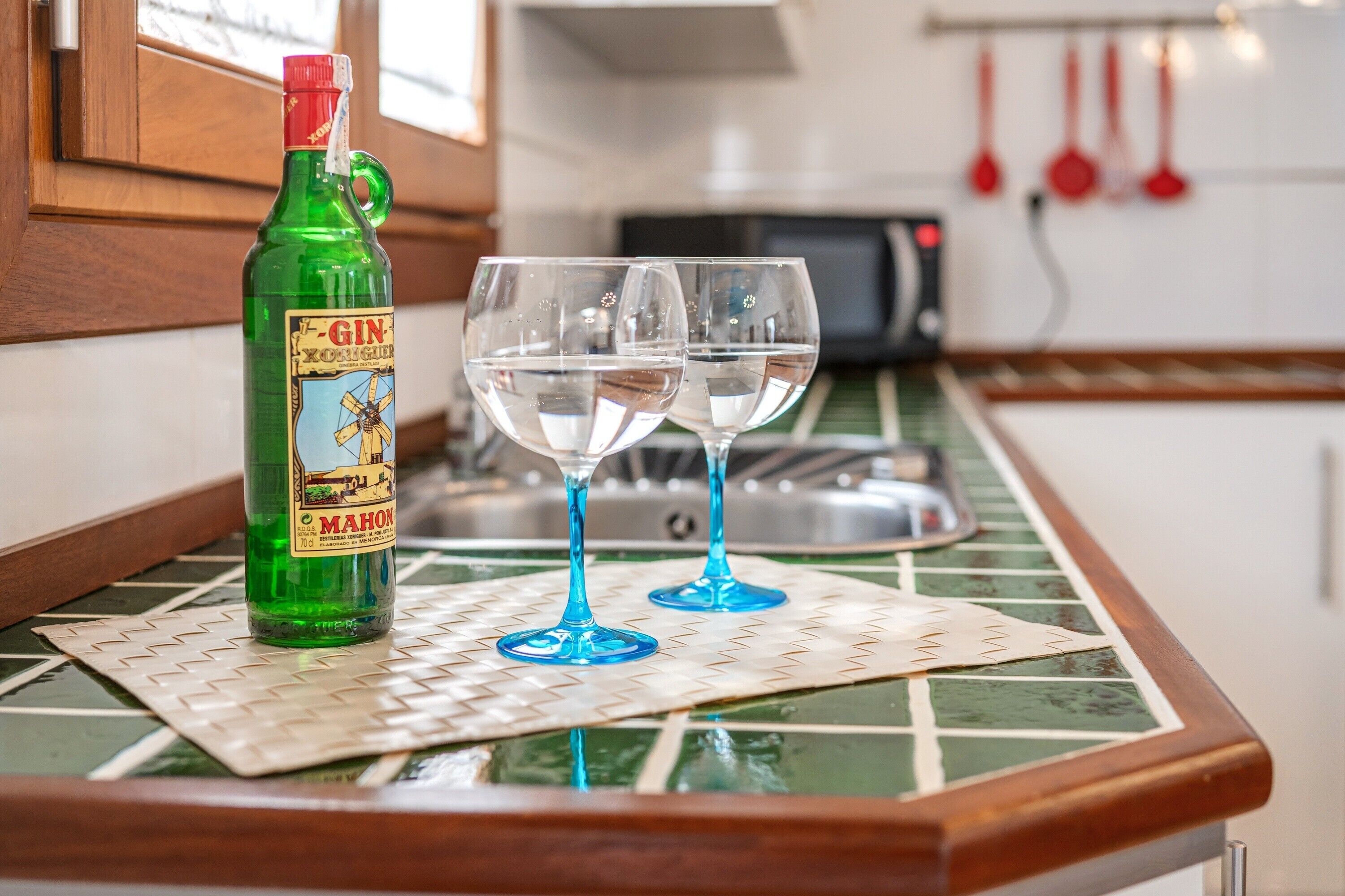 Una cuina amb un taulell, una ampolla de ginebra, dues copes i un microones.