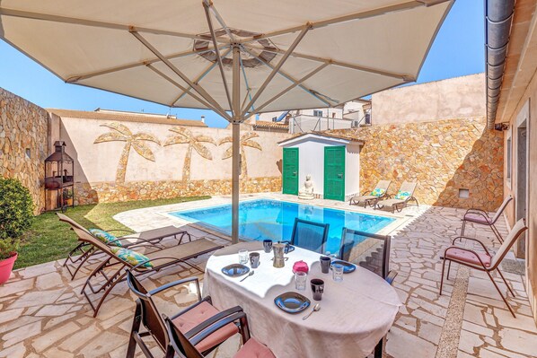 Ein Poolbereich mit Esstisch, Liegestühlen und einer Steinwand mit Palmenmotiven.