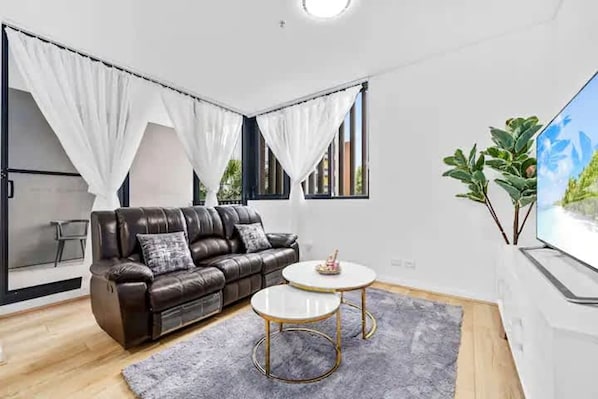 Una sala de estar moderna con un sofá de cuero, dos mesas redondas y un ventanal con cortinas blancas.