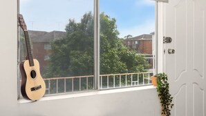 A room with a large window, a guitar leaning against the window, and a potted plant on the windowsill. - Metawise BnB 2BR Hillsdale Family Stay Sleeps 6 (Sydney)