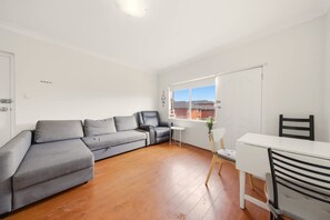 A modern living room with a grey sectional sofa, a small white table, and a white desk with a chair. - Metawise BnB 2BR Hillsdale Family Stay Sleeps 6 (Sydney)