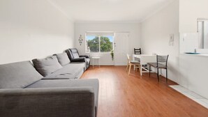 A modern, minimalistic living room with a grey sofa, a small white table, and a wooden floor. - Metawise BnB 2BR Hillsdale Family Stay Sleeps 6 (Sydney)