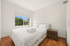 A modern bedroom with a large window, a wooden floor, a bed with white bedding, and a wooden nightstand. - Metawise BnB 2BR Hillsdale Family Stay Sleeps 6 (Sydney)