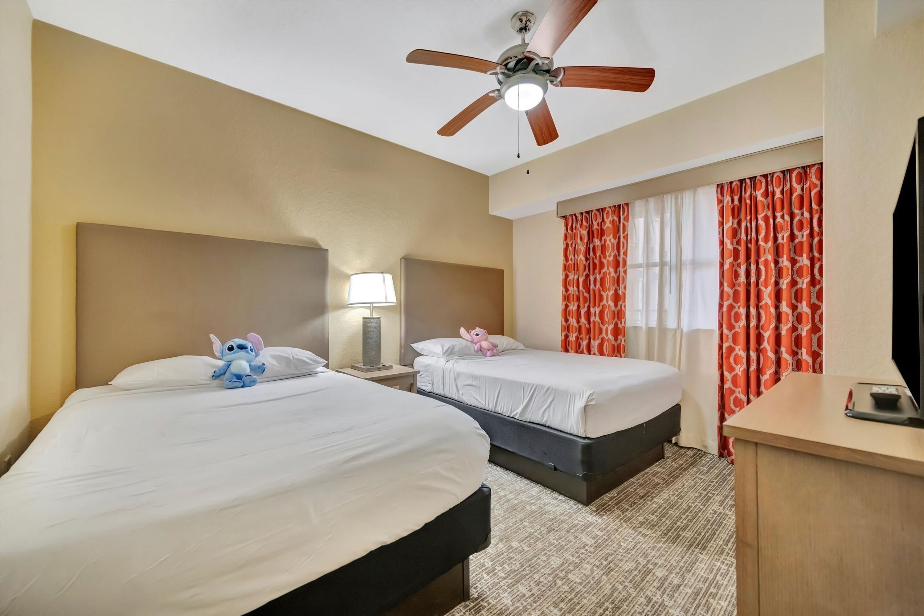 A hotel room with two beds, a ceiling fan, a TV, and a desk.