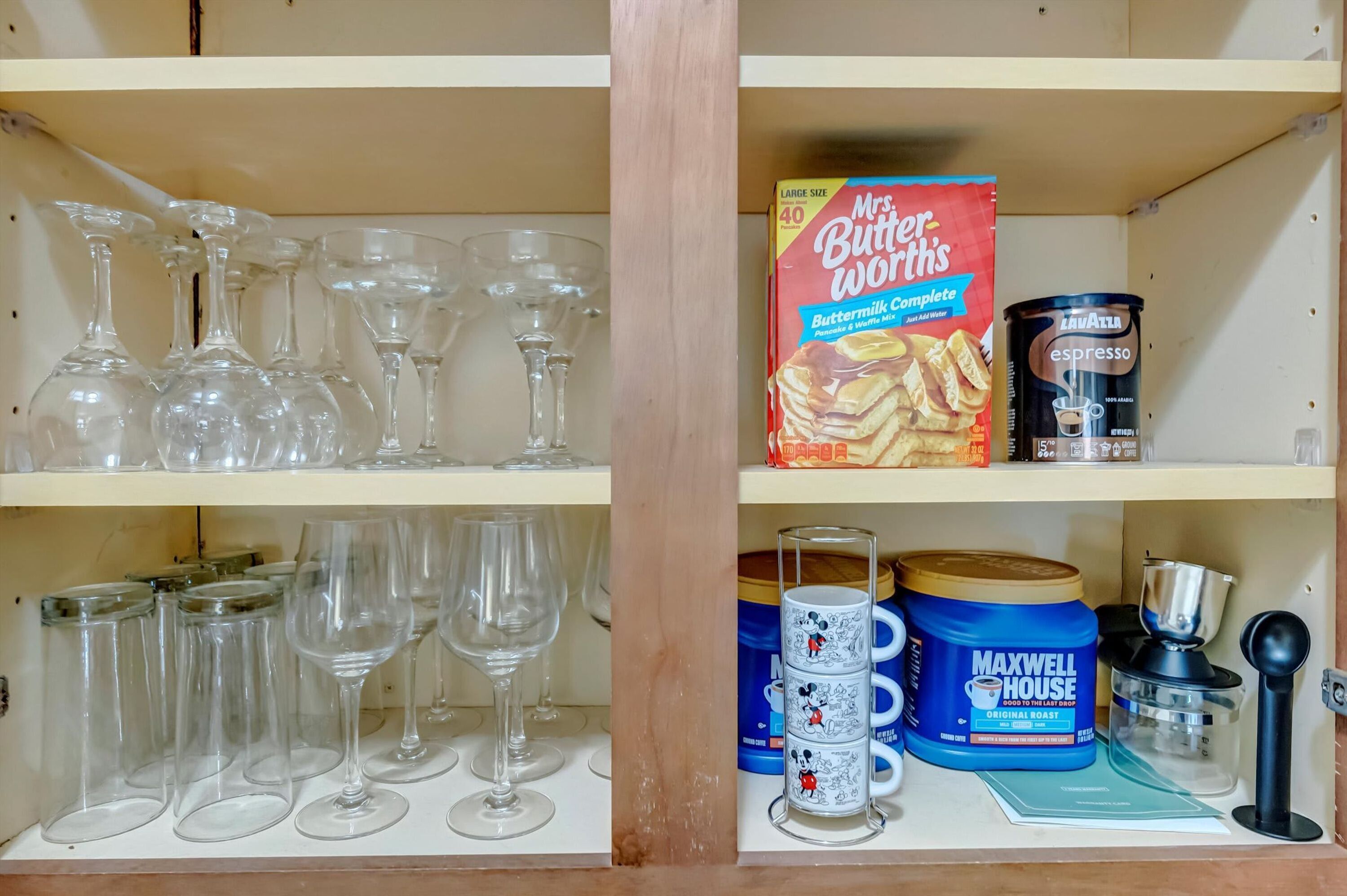 A shelf with various items including a box of Mrs. Butterworth's Buttermilk Complete, a can of Lawatta espresso, and a Maxwell House coffee maker.