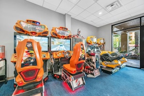 A row of arcade racing games with 'Super Cars' branding, a blue carpeted floor, and a view of the outdoors through a glass door. - Free Breakfast Parking 2B Disney Resort Condo (Orlando)