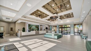 Een ruime lobby met een receptiebalie, een zithoek en een groot raam dat voor natuurlijk licht zorgt.