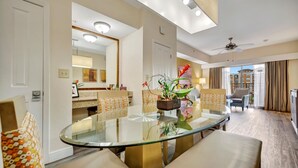 Een moderne hotelkamer met een ronde glazen tafel, beige banken, een potplant en uitzicht op de stad.