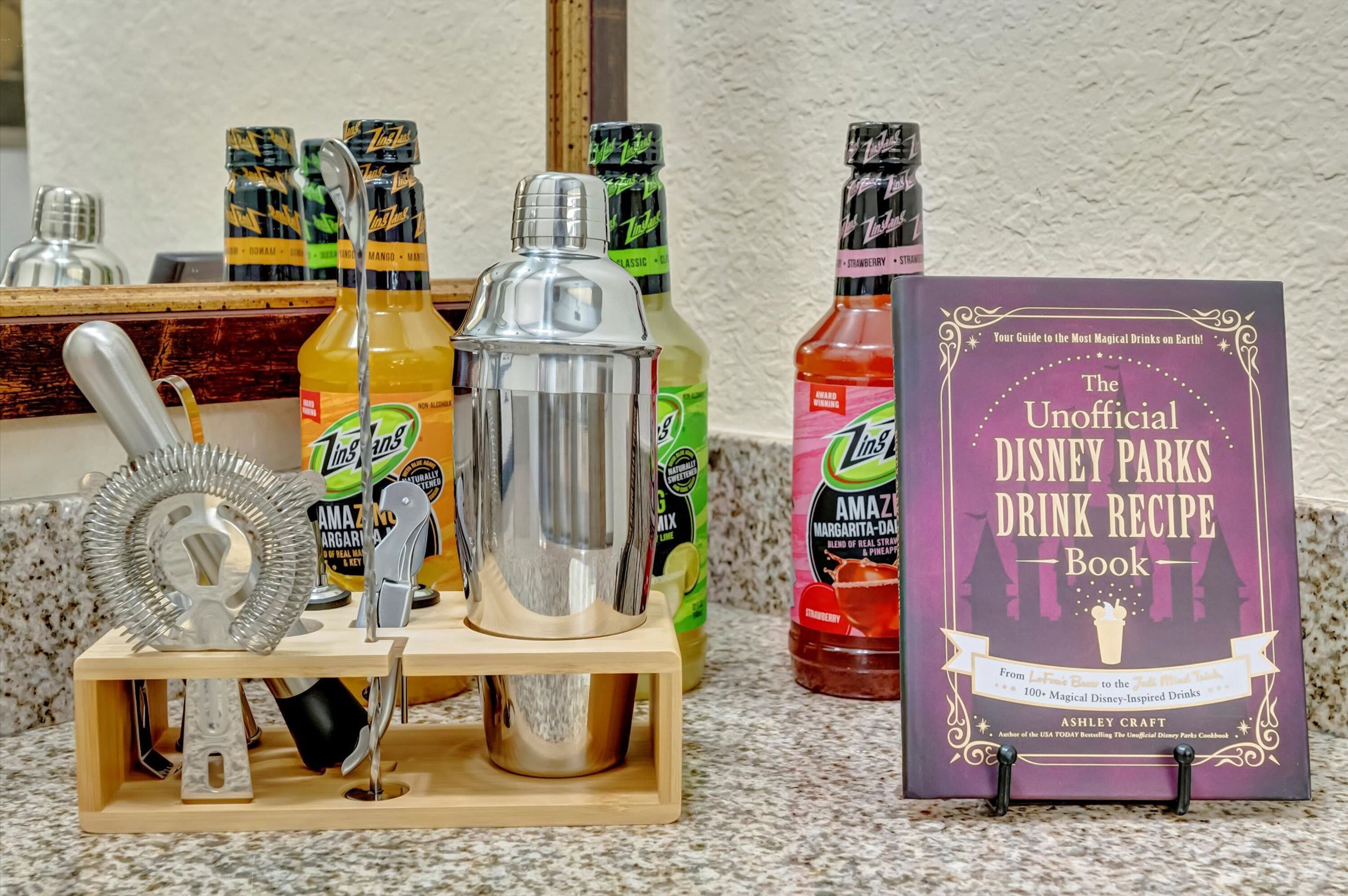 Egy konyhapult, rajta egy koktélrázó, egy üveg Limes, egy üveg Amstel sör, és egy könyv, melynek címe: „A Disney parkok hivatalosan nem kiadott italkeverési receptkönyve”.