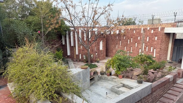Une cour avec un mur en briques, des plantes en pot et un banc en pierre.